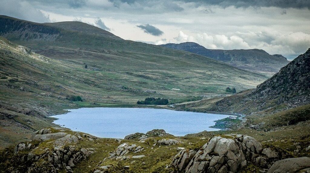 Lac de montagne encaissé entre des versants rocheux sous un ciel nuageux
