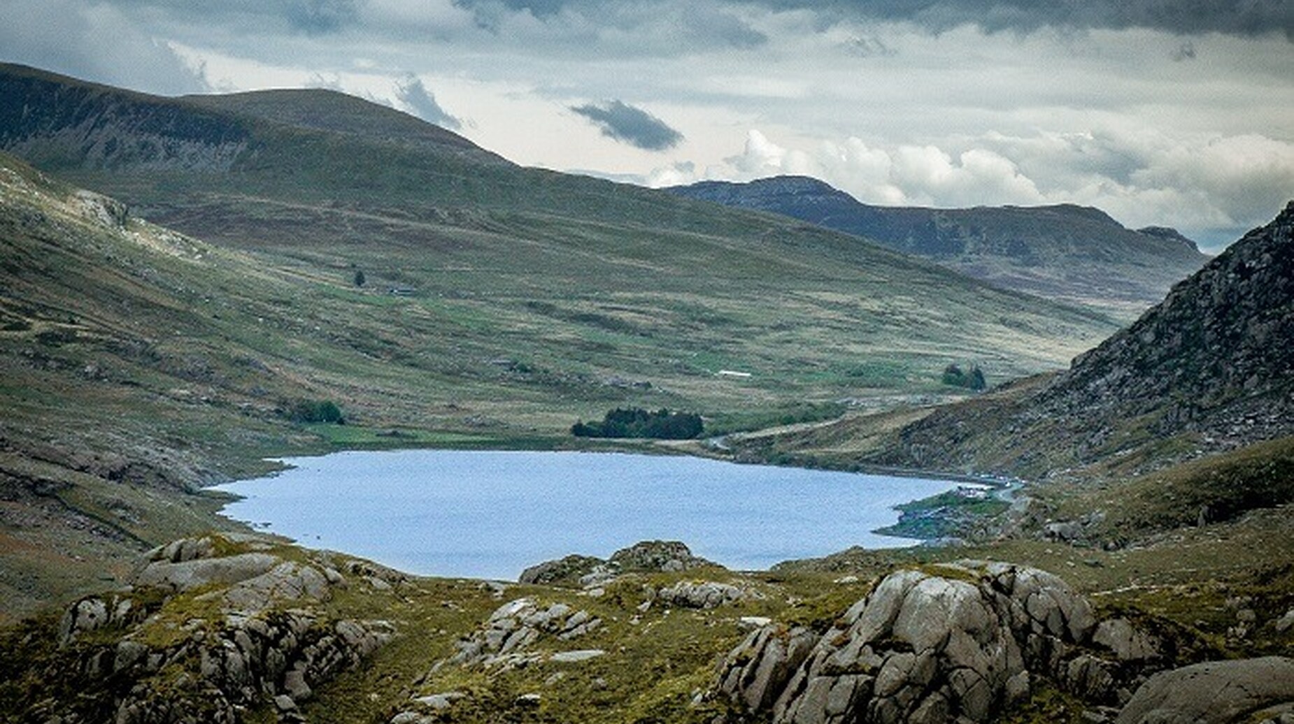 Lac de montagne encaissé entre des versants rocheux sous un ciel nuageux