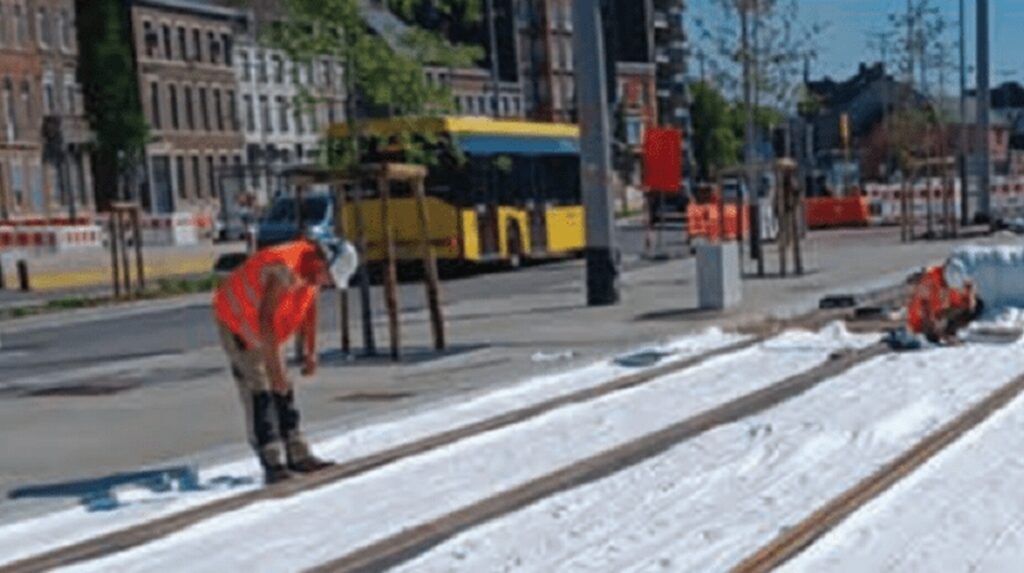 Ouvrier en tenue orange travaillant sur la pose de rails de tramway en ville