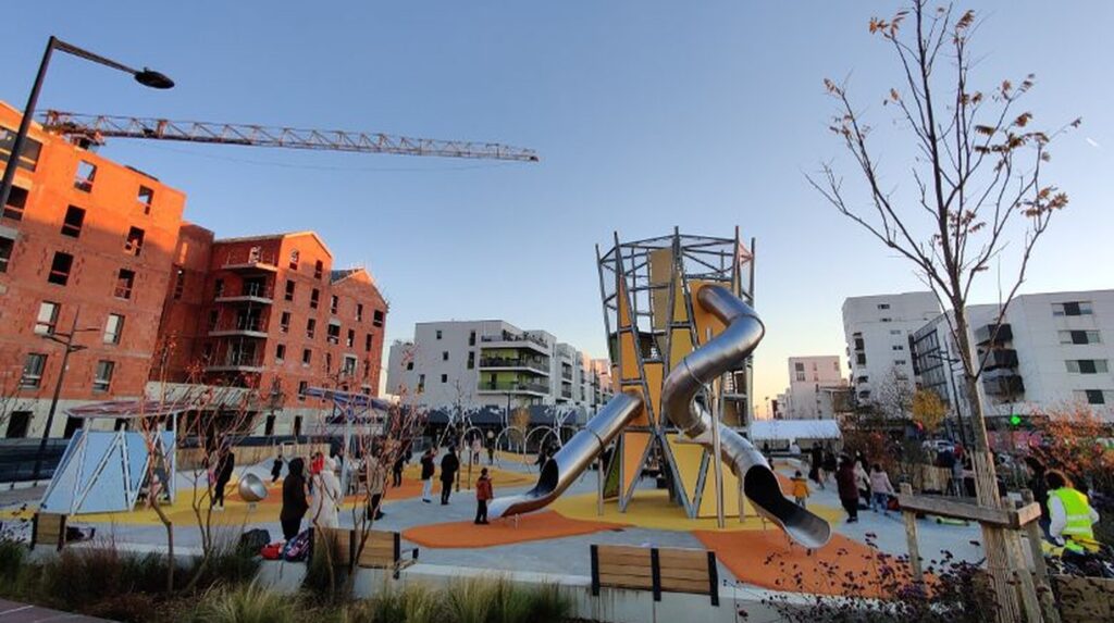 Aire de jeux animée avec toboggan métallique devant des immeubles en construction