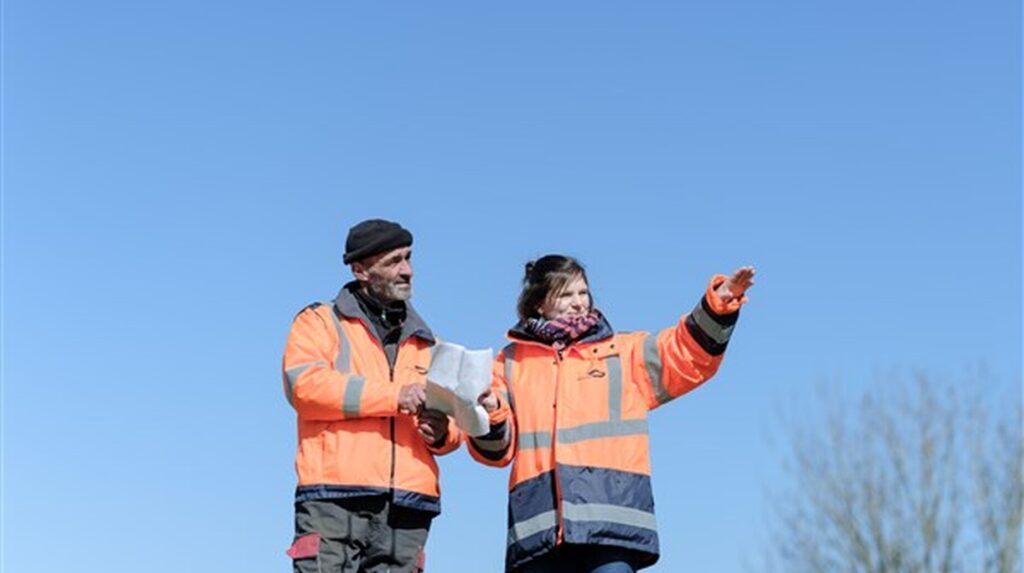 Deux professionnels du paysage en veste orange échangeant sur un site dégagé