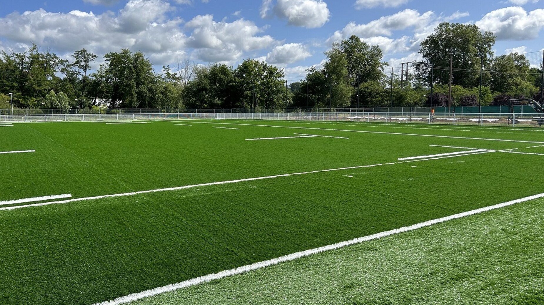 Terrain de sport en gazon synthétique entouré de clôtures et d'arbres